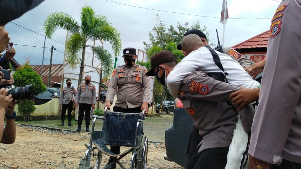 Personel Kepolisian Sultra saat menggendong salah seorang penyandang disabilitas untuk didudukan di kursi rodanya untuk menjalani vaksinasi di Polsek Mandonga Kendari.