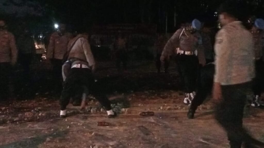 Personel polisi membersihkan kayu dan batu sisa unjuk rasa di sekitar Polda Sultra.