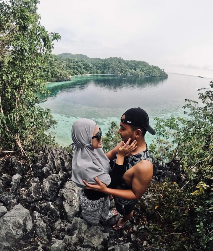 Sepasang kekasih mengabadikan momen berfoto bersama dengan view Teluk Cinta dari atas bukit.